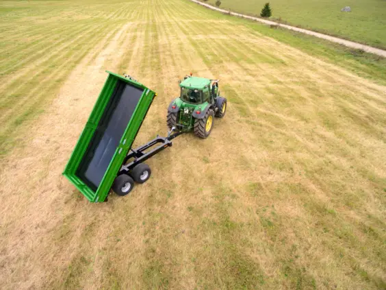 Grønn traktor med en Palmse Trailer PT150 kornhenger i tipp-posisjon på en åker.