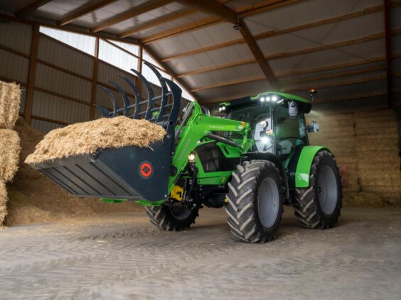 En grønn Deutz-Fahr Series 5 traktor med frontlaster som løfter fôr i en låve.