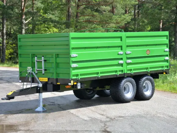 En grønn Palmse Trailer PT150 kornhenger parkert på en asfaltvei med skog i bakgrunnen.