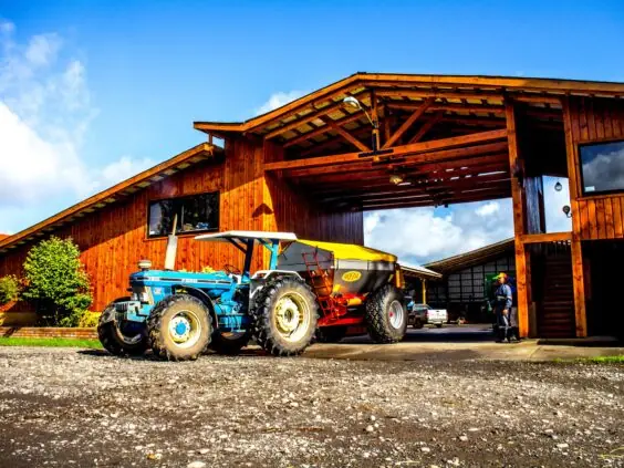 En blå Ford traktor med en Bredal kalkspreder foran en trebygning.