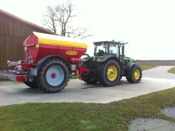 En grønn traktor med en rød og gul Bredal kalkspreder parkert utendørs.