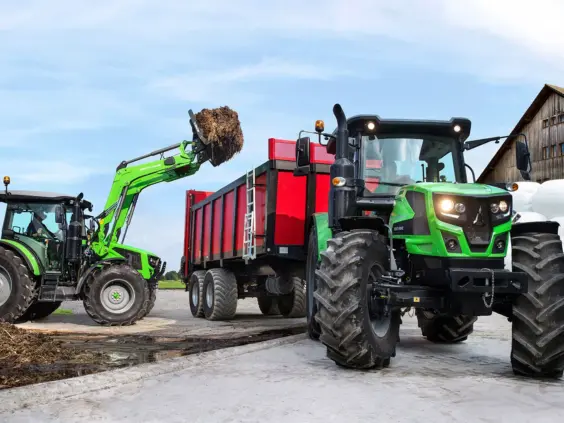 Grønn Deutz-Fahr Series 5 Keyline traktor som laster gjødsel i en rød tilhenger på gård.