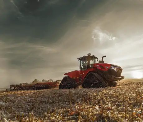 Rød Steiger 785 Quadtrac traktor som trekker landbruksutstyr over en åker ved solnedgang.