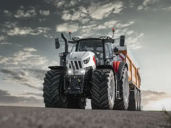 En hvit og rød Steyr Cervus CVT traktor med tilhenger på vei under dramatisk himmel.