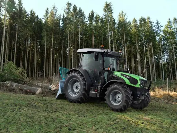 Grønn Deutz-Fahr Series 5D traktor som trekker tømmerstokker foran en tett skog.