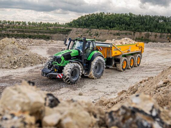 Grønn Deutz-Fahr Series 9 traktor med gul tilhenger i et travelt steinbrudd.