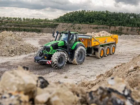 Grønn Deutz-Fahr Series 9 traktor med gul tilhenger i et travelt steinbrudd.