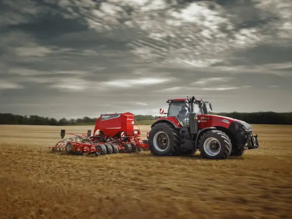 Rød Case IH traktor fra Magnum-serien i arbeid på en åker med en såmaskin.