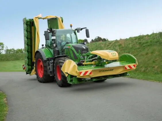 Grønn traktor med Krone EasyCut F 280 – F 320 frontslåmaskin på en asfaltvei.