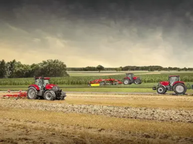 Tre røde Case IH-traktorer fra Puma-serien i arbeid på en åker under en dramatisk himmel.