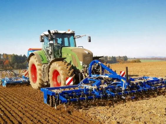 Grønn traktor i arbeid på åkeren med en blå DALBO Levelflex, fronttrommel montert foran.