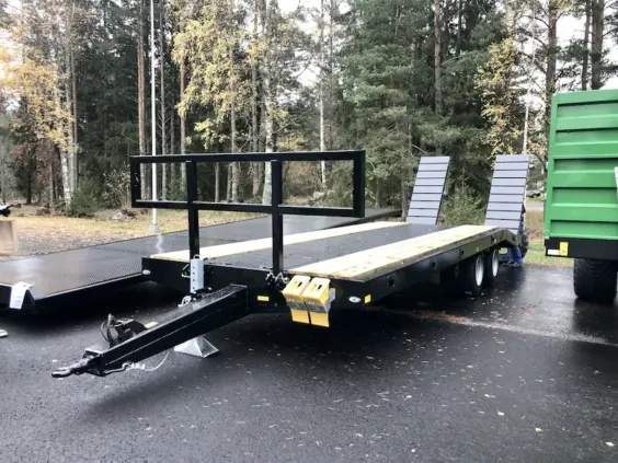 Svart Palmse PT5750 maskinhenger med tredekk og ramper, parkert på våt asfalt.