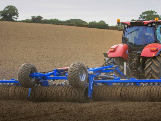 Rød traktor som trekker en DALBO Maxiroll, fleksibel systemtrommel over en åker.