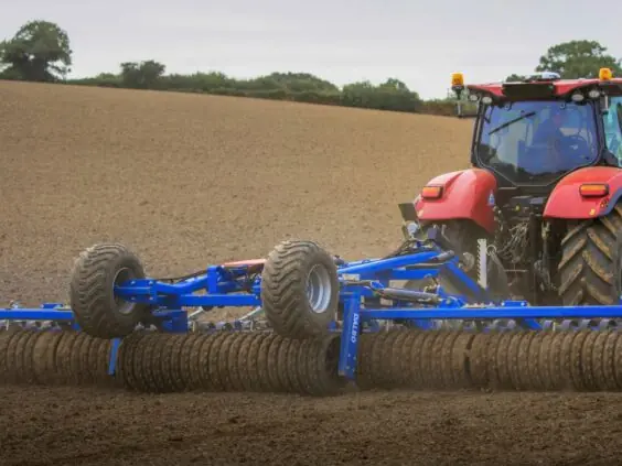 Rød traktor som trekker en DALBO Maxiroll, fleksibel systemtrommel over en åker.