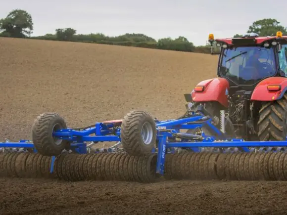 Rød traktor som trekker en DALBO Maxiroll, fleksibel systemtrommel over en åker.