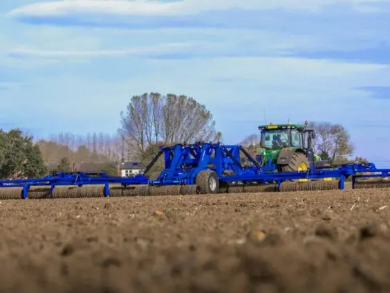 En grønn traktor trekker en DALBO Megaroll, en fullhydraulisk trommel over en åker.