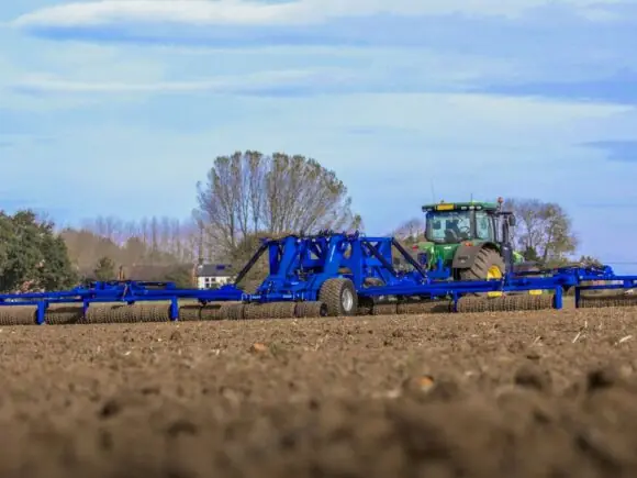 En grønn traktor trekker en DALBO Megaroll, en fullhydraulisk trommel over en åker.