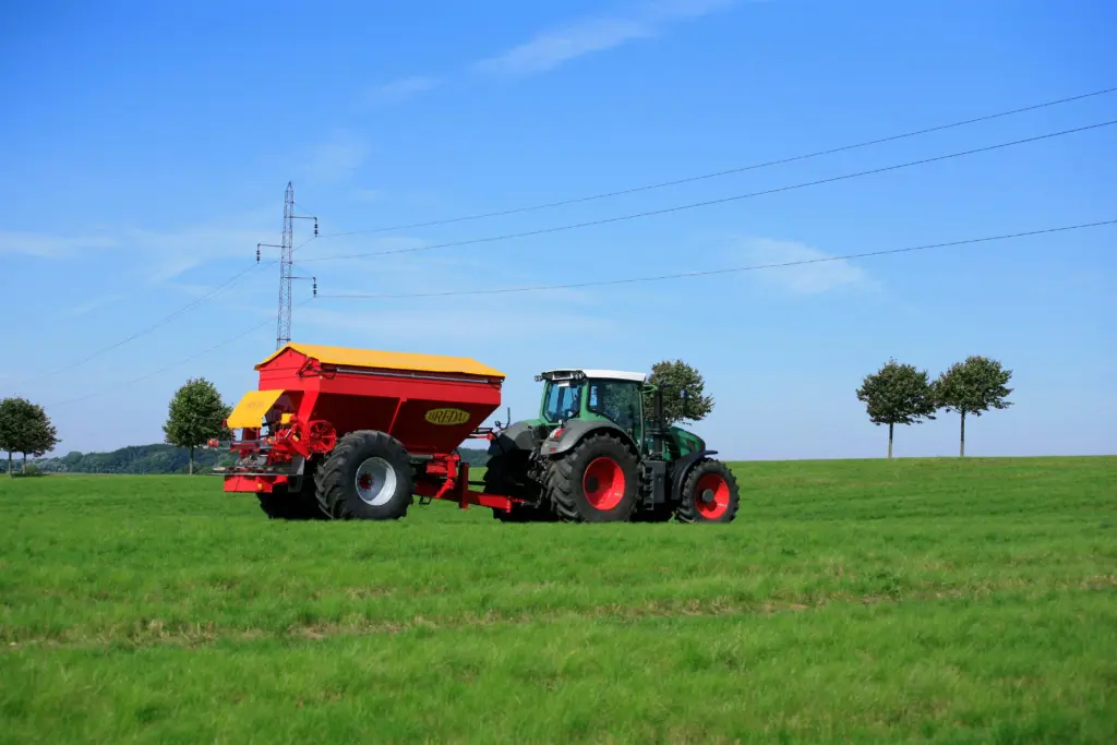 Grønn traktor med en rød og gul Bredal kalkspreder på et grønt jorde.