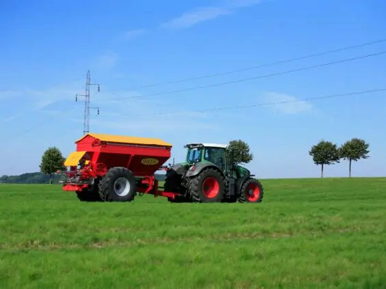 Grønn traktor med en rød og gul Bredal kalkspreder på et grønt jorde.
