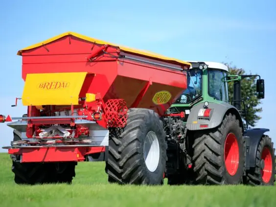 En rød Bredal kalkspreder montert bak en grønn traktor på et grønt jorde.