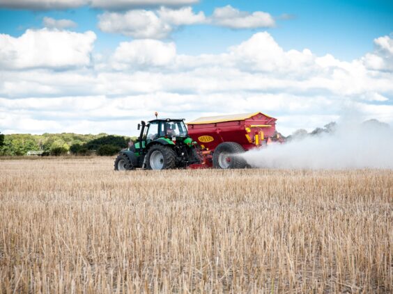 En traktor trekker en Bredal kalkspreder som sprer hvit kalk på en stubbåker.
