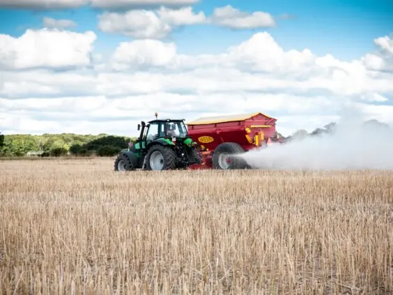 En traktor trekker en Bredal kalkspreder som sprer hvit kalk på en stubbåker.
