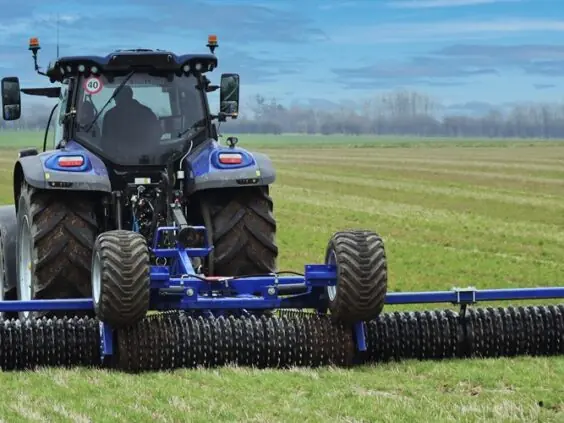 En blå traktor som trekker DALBO Minimax, en allsidig og kompakt trommel på åkeren.