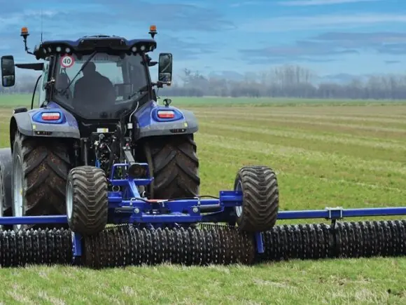 En blå traktor som trekker DALBO Minimax, en allsidig og kompakt trommel på åkeren.