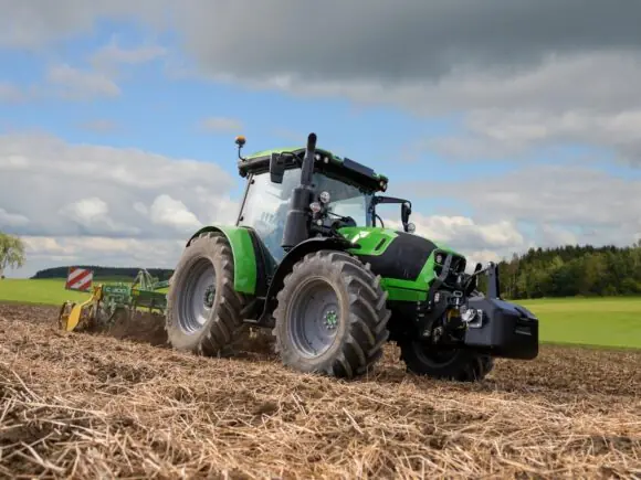 Grønn Deutz-Fahr Series 5 traktor i arbeid på en åker under en blå himmel.