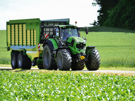 En grønn Deutz-Fahr Series 8 traktor som trekker en stor tilhenger langs en landevei.