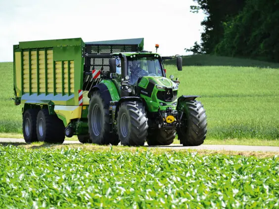 En grønn Deutz-Fahr Series 8 traktor som trekker en stor tilhenger langs en landevei.