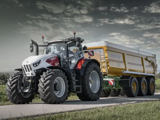 En moderne hvit og rød Steyr Cervus CVT traktor som trekker en stor gul Joskin tilhenger.
