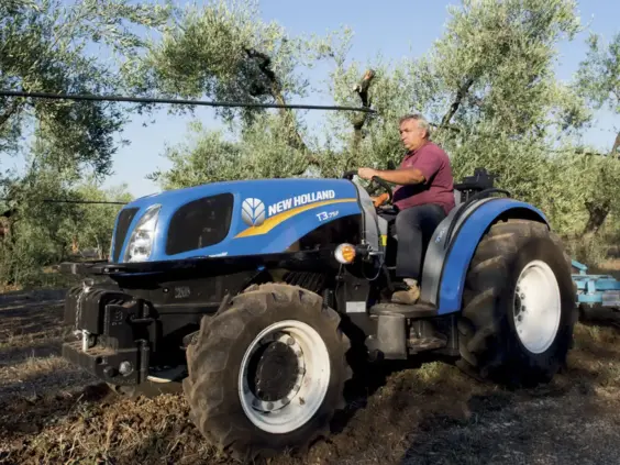 En blå New Holland traktor fra T3F-serien i arbeid i en frukthage.
