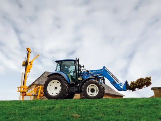 Blå New Holland T5 Utility traktor med frontlaster og stolpedriver på et grønt jorde.