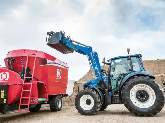 New Holland T5 Utility med frontlaster som laster en rød Kongskilde fôrblander på en gård.