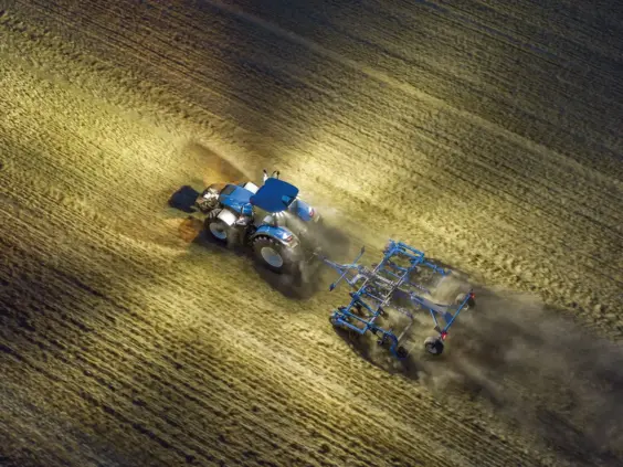 En blå T7 Heavy Duty traktor som arbeider på en åker i kveldsmørket.