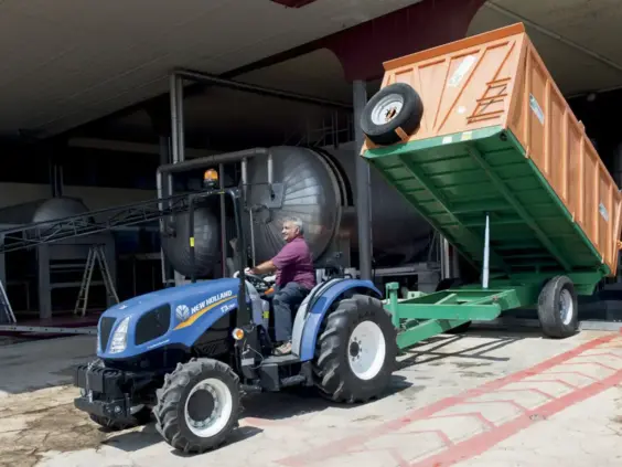 En blå New Holland traktor fra T3F-serien med en stor oransje tipphenger.