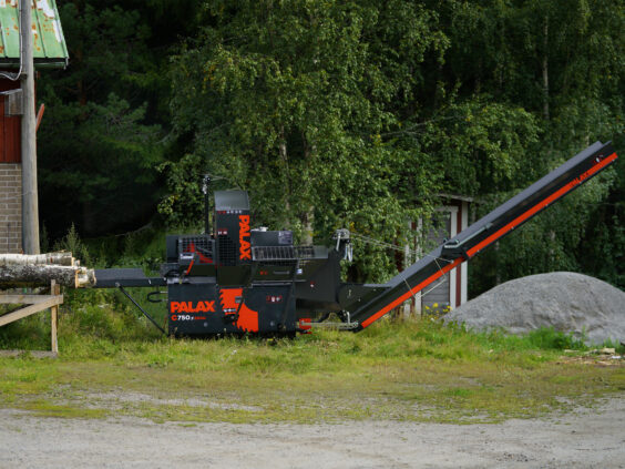 En svart og oransje Palax C750.2 vedmaskin plassert utendørs ved en tømmerstokk.