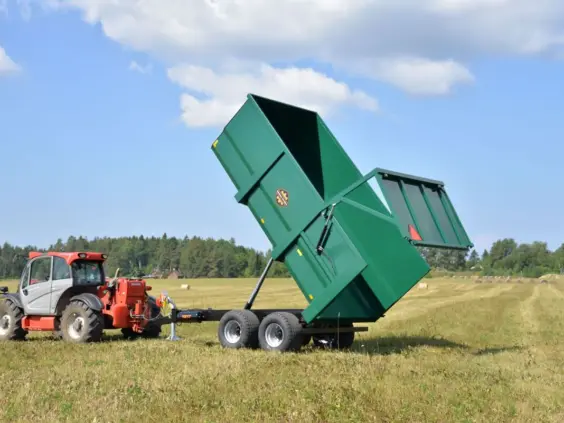 En grønn Palmse PT1217 dumperhenger tippet opp på et jorde bak en rød traktor.