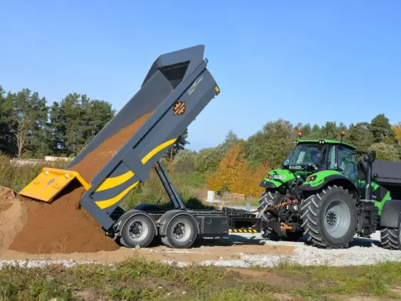 En grønn traktor med en Palmse PT1610E-PS-TE50 dumperhenger som tipper jord utendørs.