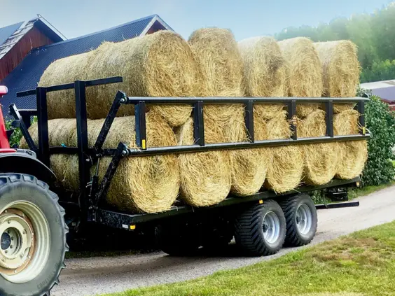 En Palmse PT3750PS plattformhenger lastet med store rundballer av høy bak en traktor.