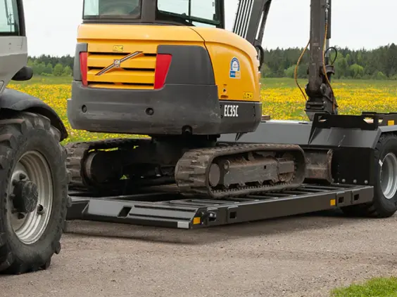 Gul gravemaskin på en Palmse PT5350 maskinhenger parkert på en grusvei.