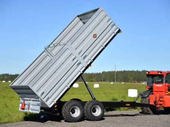 En tippet Palmse Trailer PT150 kornhenger i galvanisert stål koblet til en rød traktor.