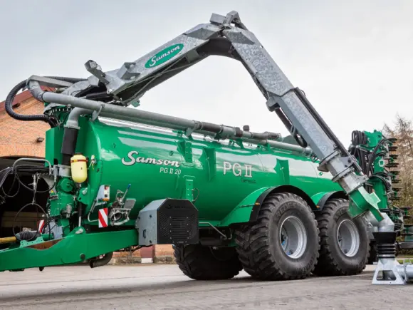 Grønn SAMSON PG II Genesis gjødselvogn med stor tank og kraftig lastearm på et gårdstun.