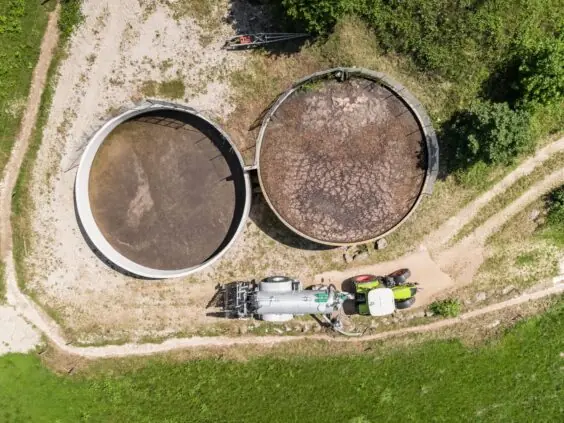 Traktor med Pichon fyllesystemer for vakumvogner ved store gjødseltanker i et landbrukslandskap.
