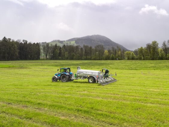 Blå traktor som trekker en Pichon SV-serien vakumvogn over en frodig grønn eng.