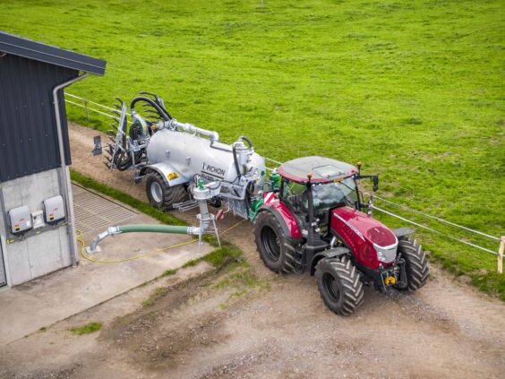 Rød traktor koblet til Pichon fyllesystemer for vakumvogner ved en landbruksbygning.