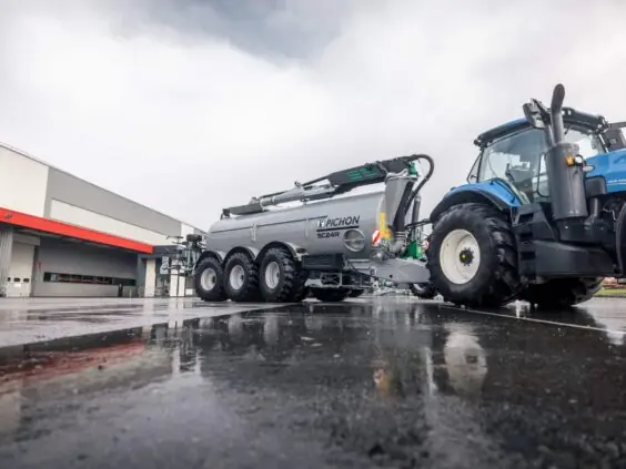 En blå traktor som trekker en grå Pichon SC24R gjødselvogn på våt asfalt.