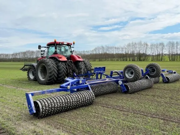 Rød traktor på jorde med DALBO Powerroll høykapasitets slepetromler under arbeid.