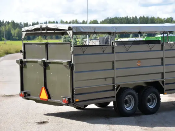 En solid grønn PT4650 dyrehenger med grå presenning parkert utendørs på en grusvei.
